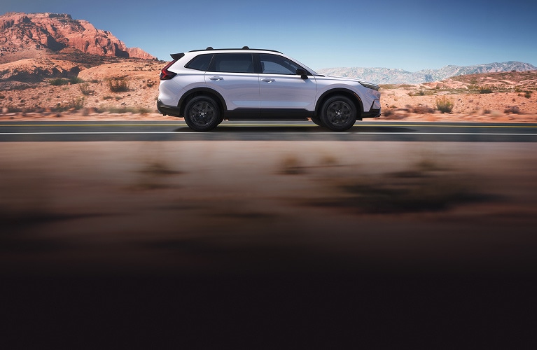 2026 Honda CR-V Sport Touring Hybrid in Platinum White Pearl profile driving on a scenic desert road (Compact Crossover SUV). 2026 Honda CR-V Sport Touring Hybrid in Platinum White Pearl profile driving on a scenic desert road (Compact Crossover SUV).