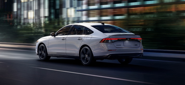 2026 Honda Accord Sport Hybrid in Platinum White Pearl rear angle driving on a dark street (Mid-Size Sedan). 2026 Honda Accord Sport Hybrid in Platinum White Pearl rear angle driving on a dark street (Mid-Size Sedan).